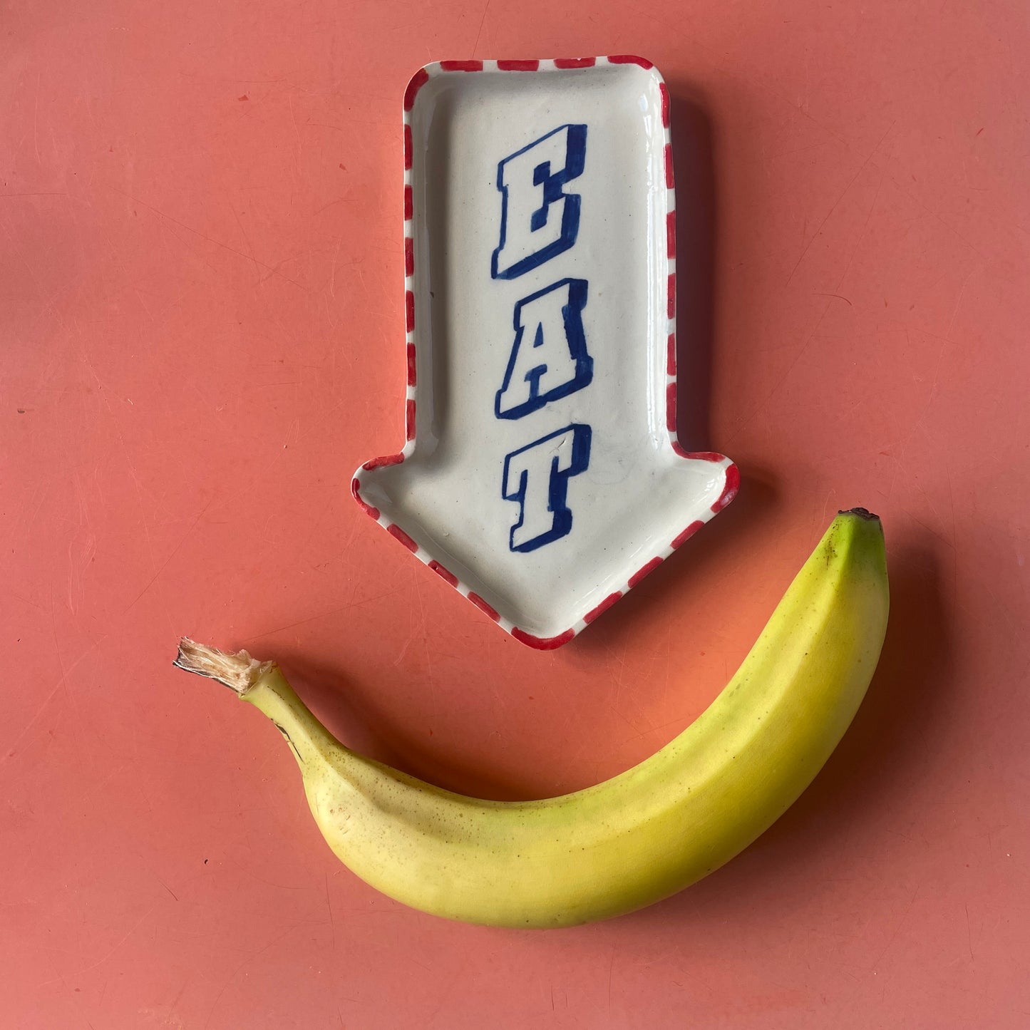 Banana with a decorative plate shaped like an arrow with 'EAT' on a red background