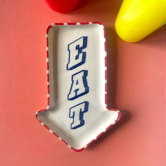Decorative plate shaped like an arrow with 'EAT' text on a pink background