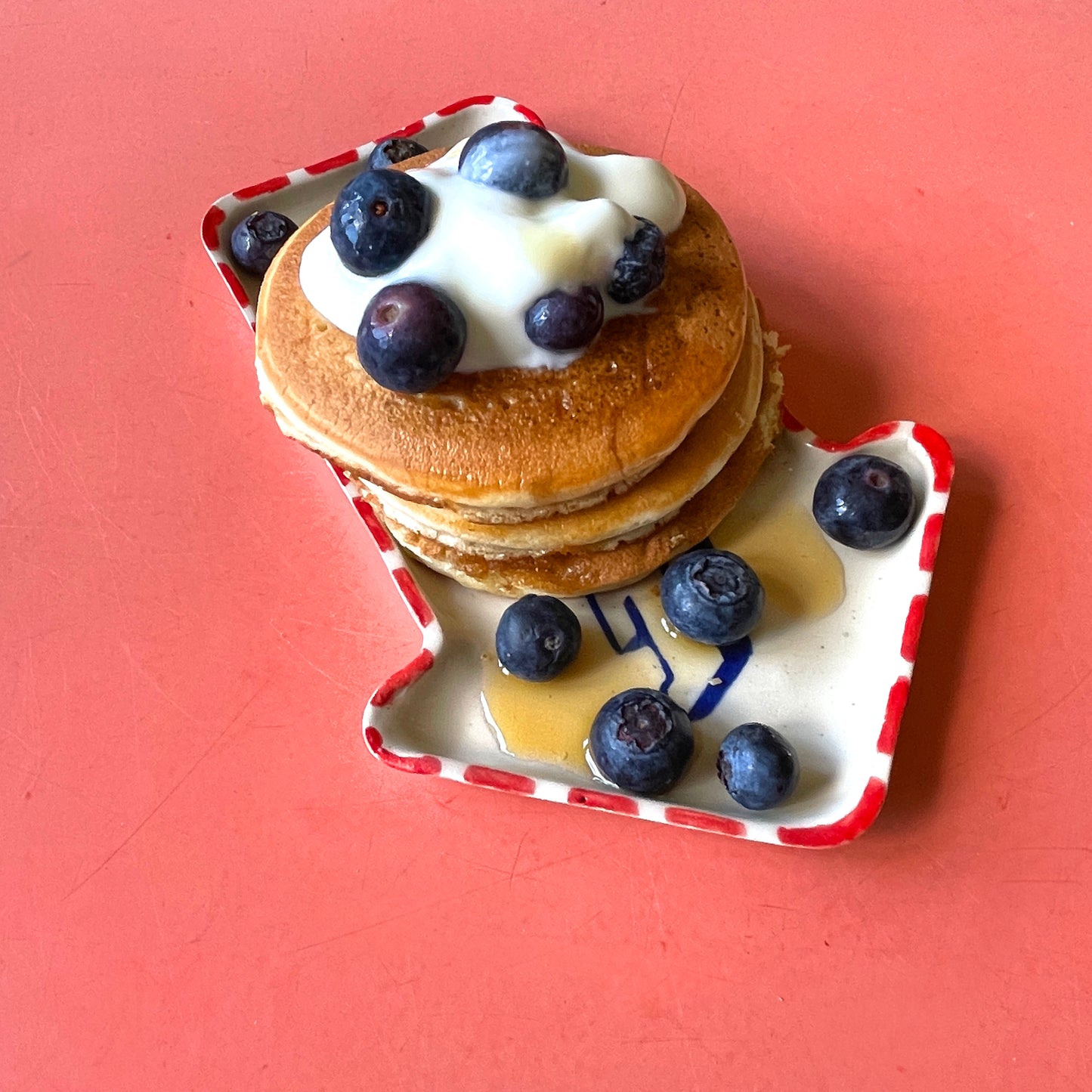 Stack of pancakes with blueberries and syrup on EAT dish against a pink background