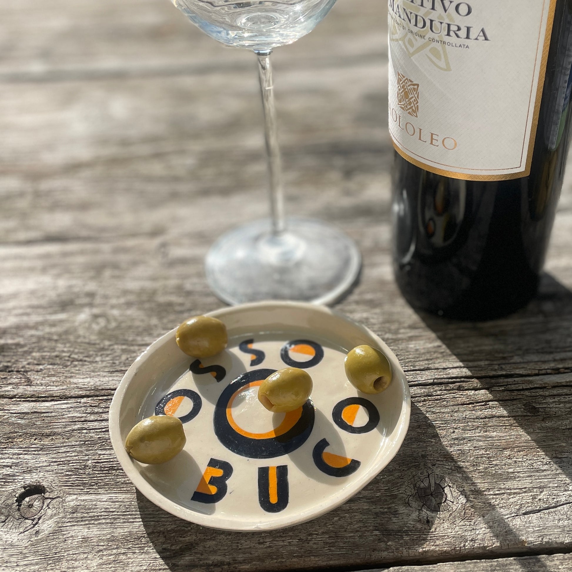 Olive dish with olives, wine glass, and bottle on a wooden surface